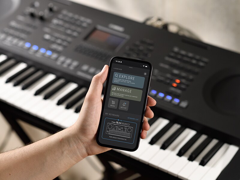 PSR-SX920 and a hand holding a smartphone with a music player screen.